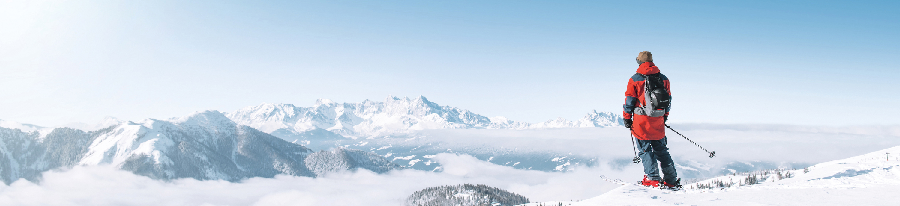 Skifahrer blickt auf verschneite Berglandschaft mit Nebel im Tal und klarblauem Himmel.