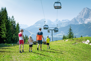 Family of four hiking on meadow near a cable car with mountain view in summer